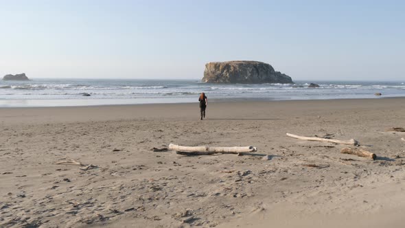 A man with long red hair runs down a beach towards the water. alt