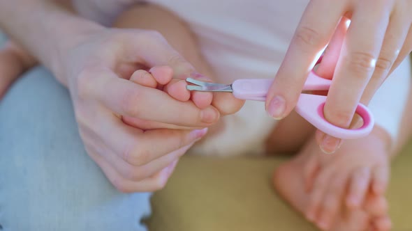 Close Up of a Woman Hands with Scissors Cuts the Toenails of a Baby alt
