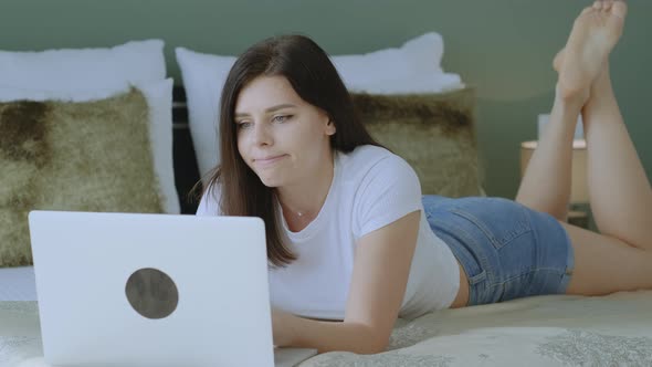 Tired Millennial woman working on laptop and closing it while lying on the bed at home