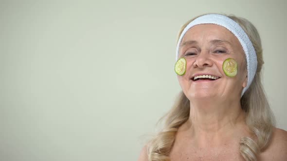 Funny Joyful Granny With Cucumber Mask on Face Biting One Slice and Smiling alt