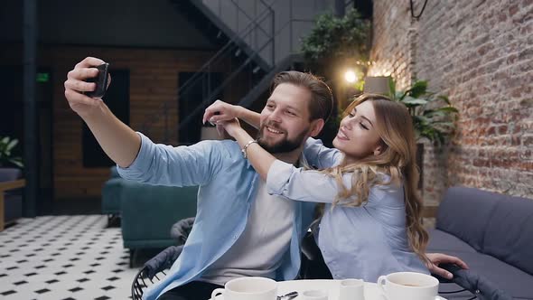Blond Woman Hugging Her Joyful Bearded Boyfriend by Neck During Making Funny Selfie alt