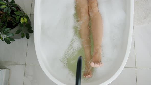 Close-up of Female Legs Moving in Bathtub Enjoying Warm Water and Foam Bubbles alt