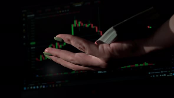 Stack of Dollars Falls Into a Hand Against the Background of a Stock Market Chart alt