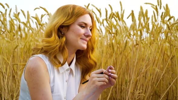Cheerful redhead girl playing with wheat ear in field in summer alt