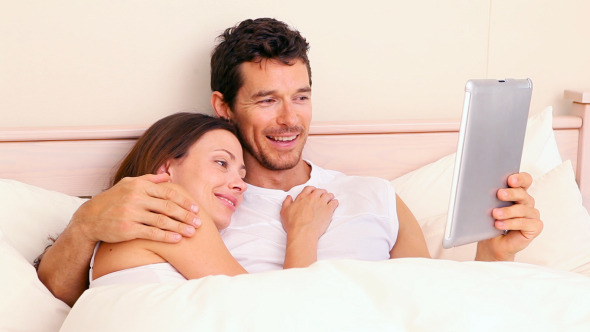 Couple Lying In Bed Using Digital Tablet