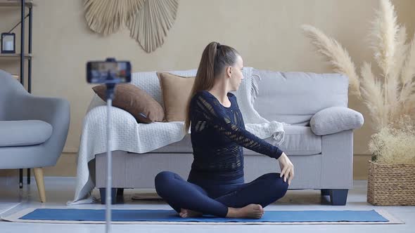 Young Yoga Blogger Woman Streaming Yoga Practice with Cellphone Camera at Home