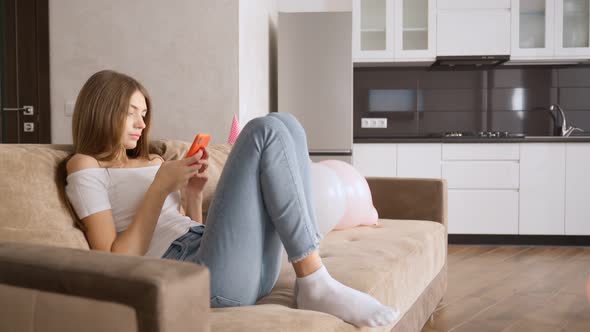 Caucasian Girl Typing Using Smartphone on Couch. alt
