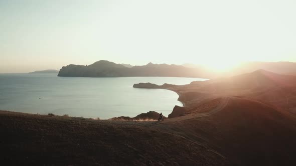 Drone View of Man on Motorbike Extremely Rides Across the Hills with Black Sea on Background in