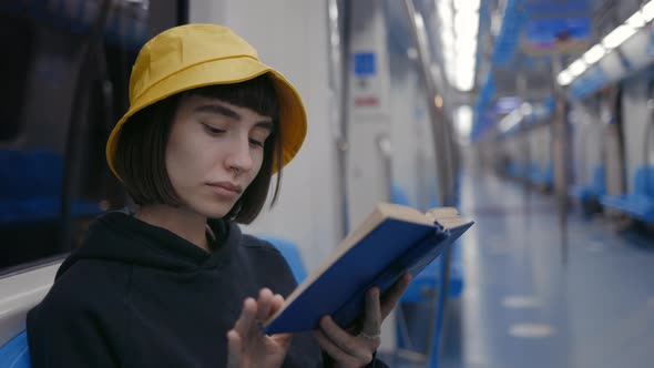 Young Woman Sitting at Subway Train and Reading Book alt