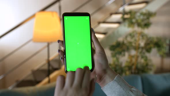 Chroma key mock-up on smartphone in hand. Woman holds mobile phone indoors of cozy home alt