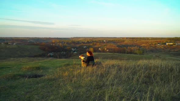 Owner and pet American Staffordshire terrier sitting on green hill at sunset alt