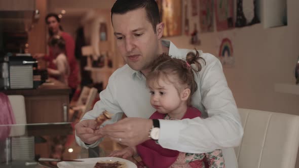 Father feeding pancake to baby girl at table