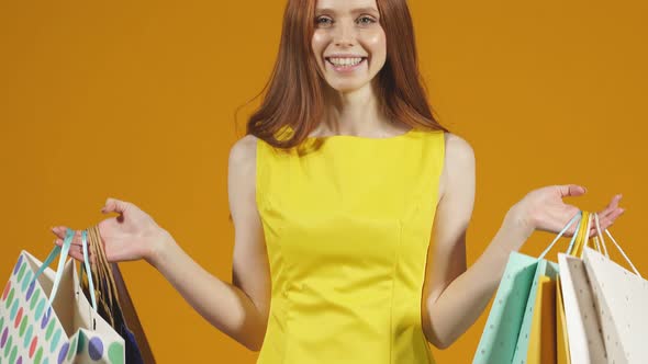 Happy Young Woman in a Bright Yellow Dress Enjoys Her Shopping While Holding a Variety of Colorful