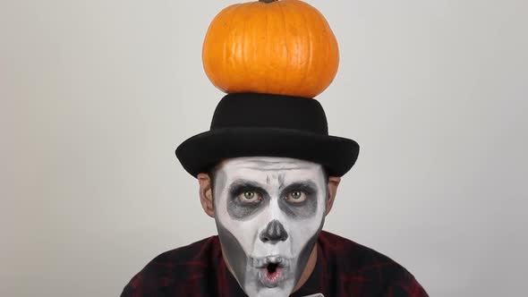 A Terrible Man in Clown Makeup and with a Pumpkin on His Head Grimaces and Waves His Hand in alt