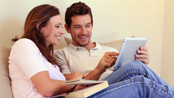 Happy Couple Sitting On Sofa Using Tablet Pc
