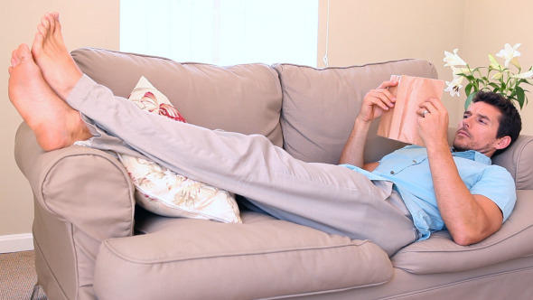 Man Lying On Couch Falling Asleep While Reading