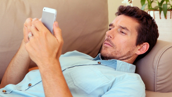 Man Lying On Couch Answering His Phone