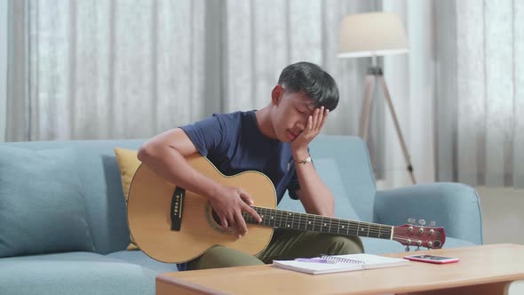 Asian Boy Composer With A Guitar Having A Headache While Composing Music At Home alt