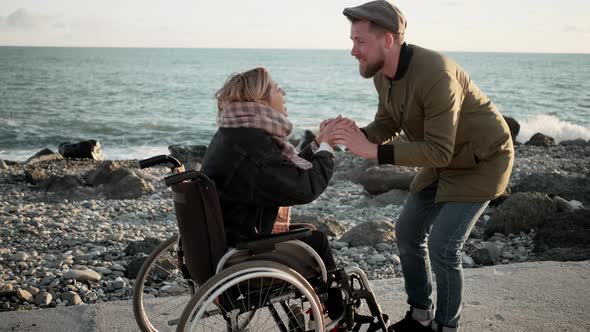 Man Is Invigorating His Beloved Woman Sitting in Wheelchair in Sea Beach alt