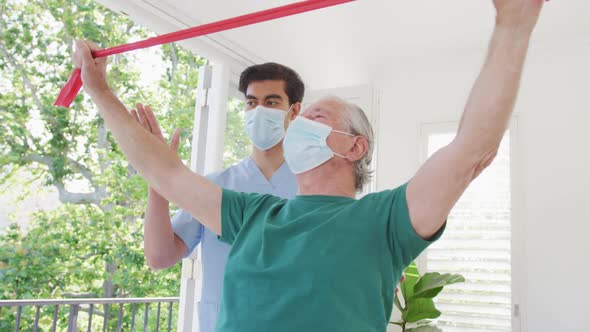 Male therapist and senior man wearing face masks while exercising at nursing home during covid alt