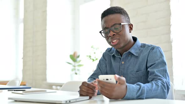 Upset Young African Man reacting to Loss on Smartphone alt