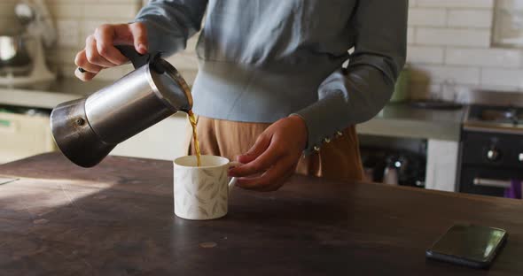 Midsection of caucasian woman standing at counter in cottage kitchen pouring coffee from pot alt