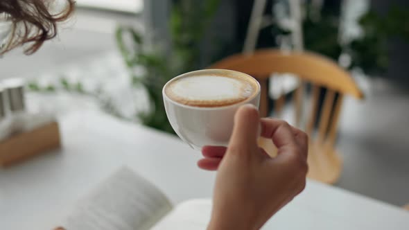 Office Worker Girl Sits At Lunch In A Restaurant Drinking Fresh Hot Cappuccino While Reading A Book alt