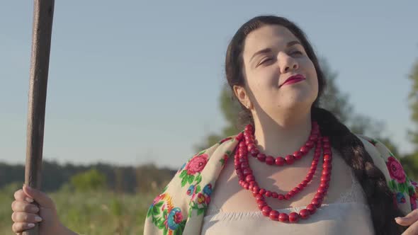 Portrait Cute Overweight Woman Holding a Scythe Looking at Camera on the Green Summer Field in alt