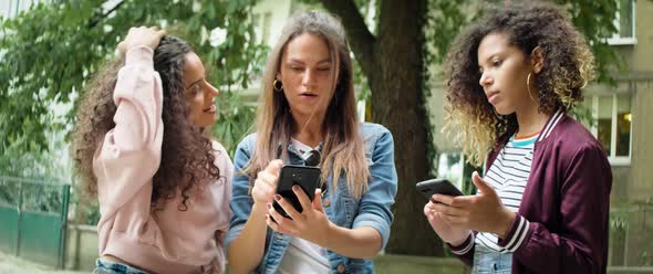 Three young friends using mobile phone outdoors. Shot with RED helium camera in 8K. alt