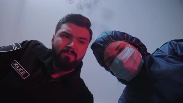 Bottom View of Police Officer and Criminologist Openin Vctim Body, Looking at Each Other, Shaking alt