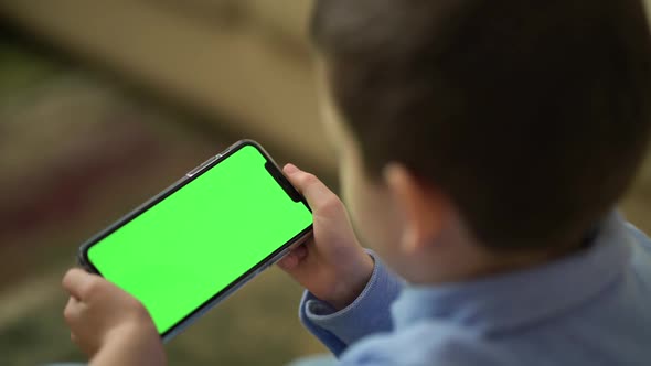 Back View of Boy Holding Phone with Chroma Key Green Screen and Watching Content alt