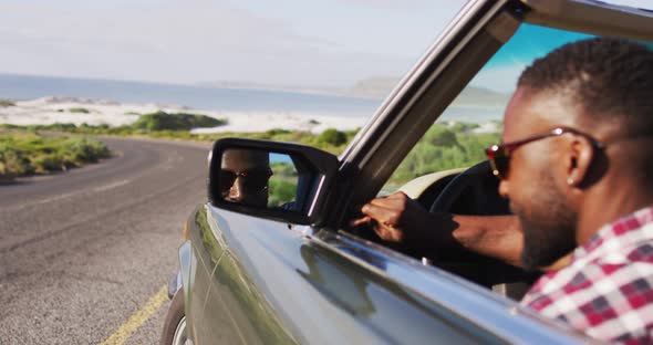 African american man adjusting side rear view mirror while sitting in convertible car alt