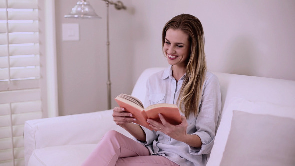 Blonde Woman Reading A Book Sitting On Couch