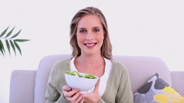 Content Blonde Woman Eating Salad Sitting On Couch