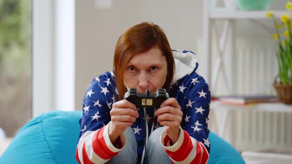Front View Absorbed Mature Woman Gaming Online with Joystick Grimacing Sitting on Bag Chair in alt