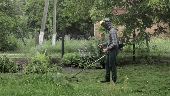 Worker mowing tall grass with electric or petrol lawn trimmer. Gardening care tools and equipment. alt