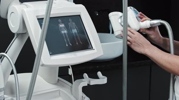 The Therapist Takes an Electric Device for Massage and Selects the Function on the Monitor alt