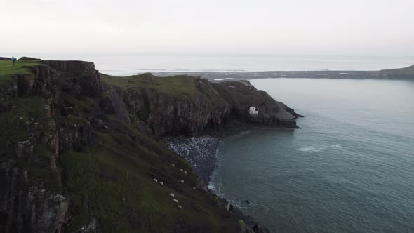 AERIAL: Fly along coastal cliffs towards abandoned boathouse, Rhossili Gower, 4k Drone alt