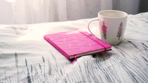 Cup of Beverage and Notebook on the Bed