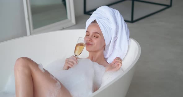 Attractive Blonde Woman with Closed Eyes of Pleasure Wrapping Head in White Terry Bath Towel Lying alt