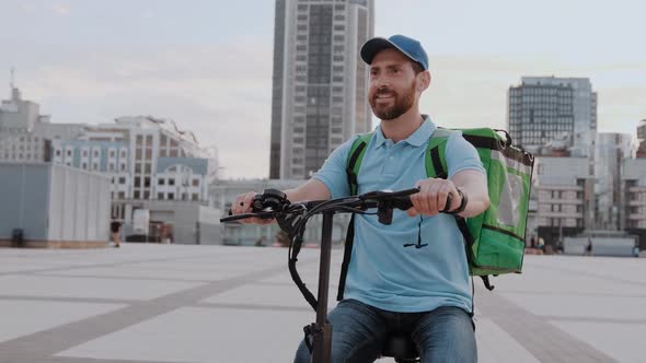 Man Courier Food Delivery with Thermal Backpack Rides the Street on an Electric Scooter Deliver alt