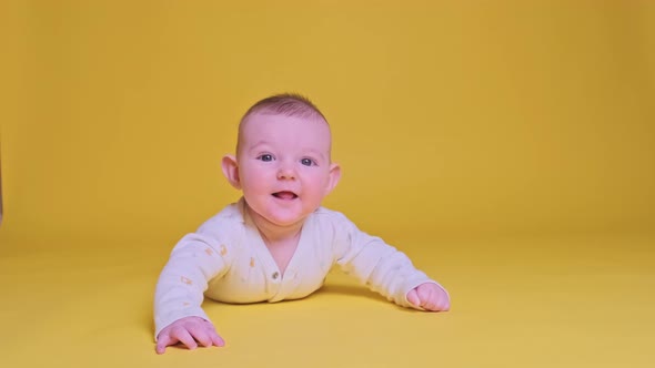 Happy infant baby boy smiling lying on his tummy, studio yellow background.