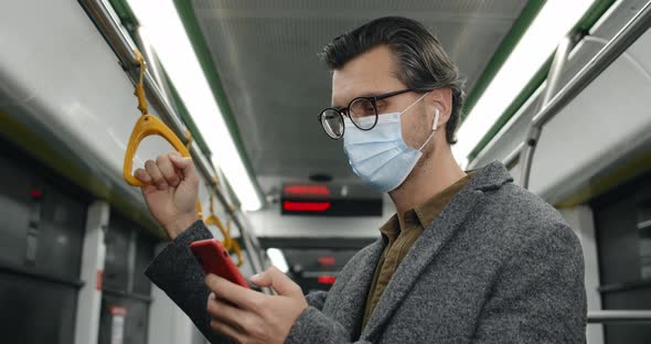 Portrait of Handsome Male Person in Medical Mask and Glasses Using Smartphone alt