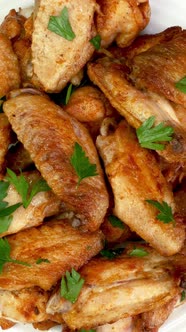 Many fried, sprinkled with parsley, sliced chicken wings rotate slowly in white plate.poultry, roast
