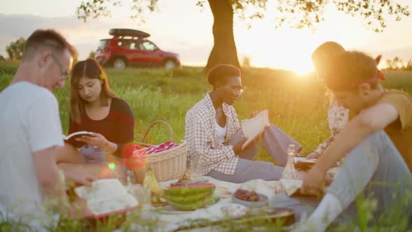 Diverse Group of Young People Study Scripture Outside in Park Picnic on Sunset