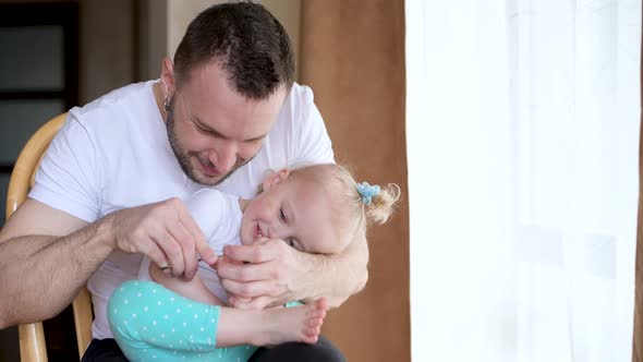 Father cuts his nails to his little daughter. Dad and baby have a great time alt