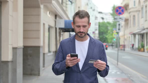 Man Shopping Online on Smart Phone While Walking Down the Street alt