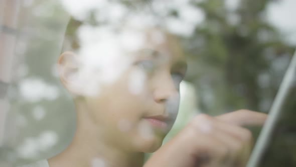 Serious Boy Sits Near the Window and Uses the Tablet, Glare in the Window