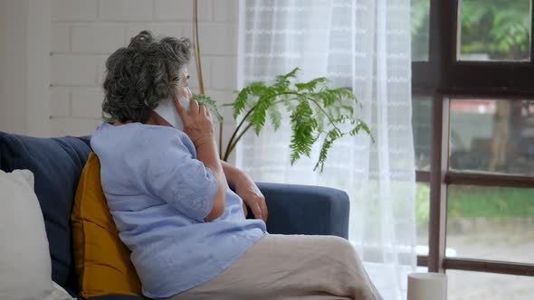 Portrait senior Asian woman talking on smartphone happy and smiling while sitting on a sofa at home.