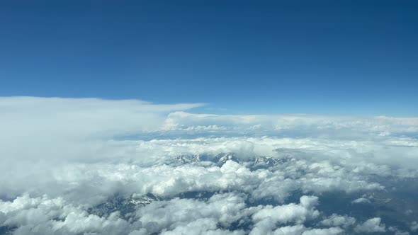 Cumulus clouds against blue sky over mountain range. Up above cloud pov airplane view alt